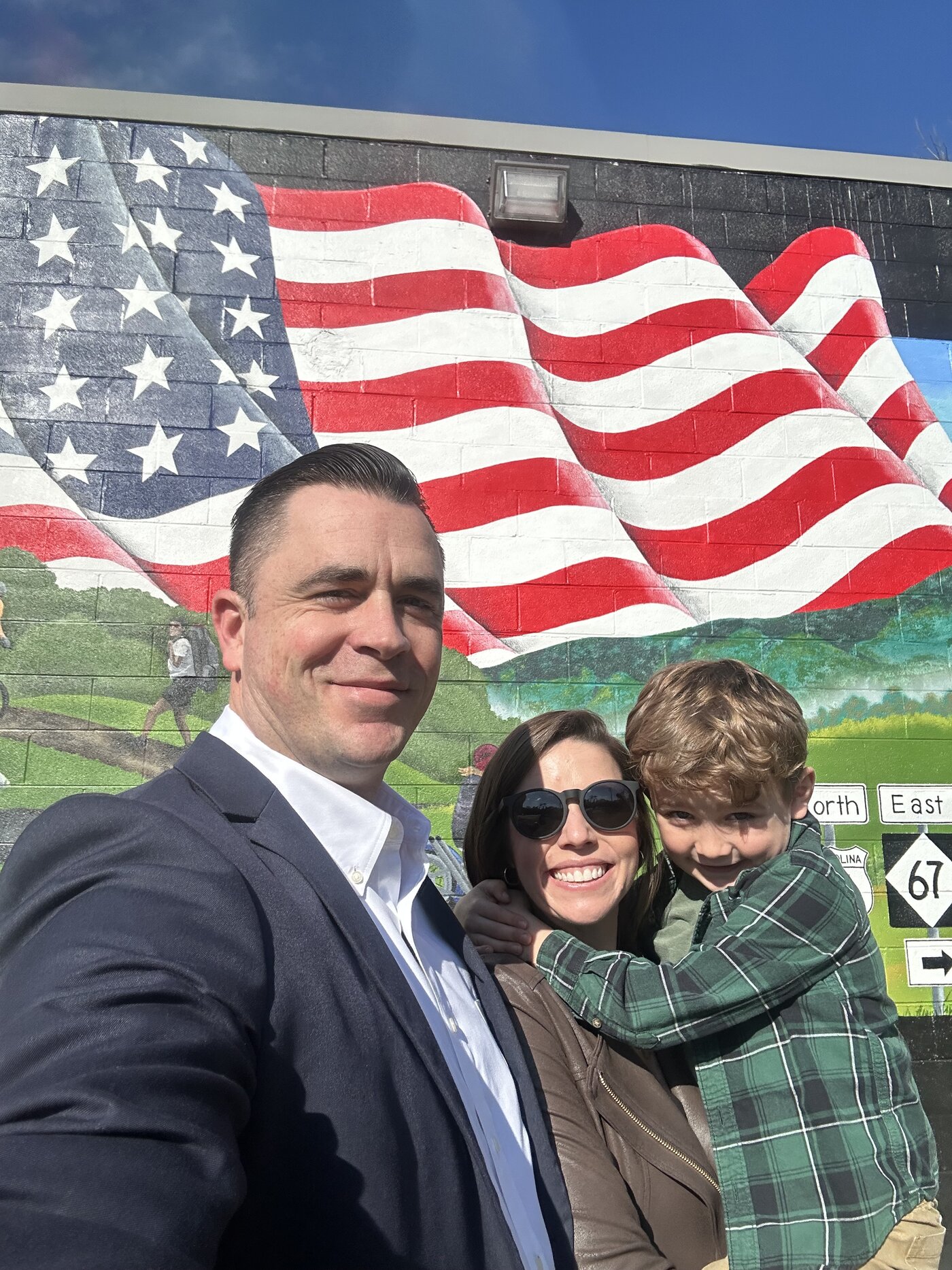 Robert Reavis with his wife and son in front of an American flag mural